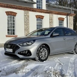 Ds-cars - Srebrny Hyundai i30 kombi na śniegu przed budynkiem z ceglanymi detalami. Zimowe opony. Wynajem aut na zimowe warunki.