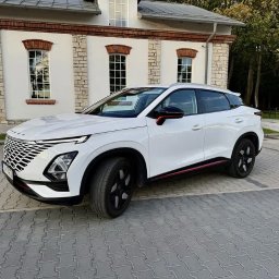 Ds-cars - Biały crossover z czarnymi felgami i czerwonym akcentem, zaparkowany na kostce brukowej przed budynkiem z ceglanymi detalami. Nowoczesny design, widok z boku.