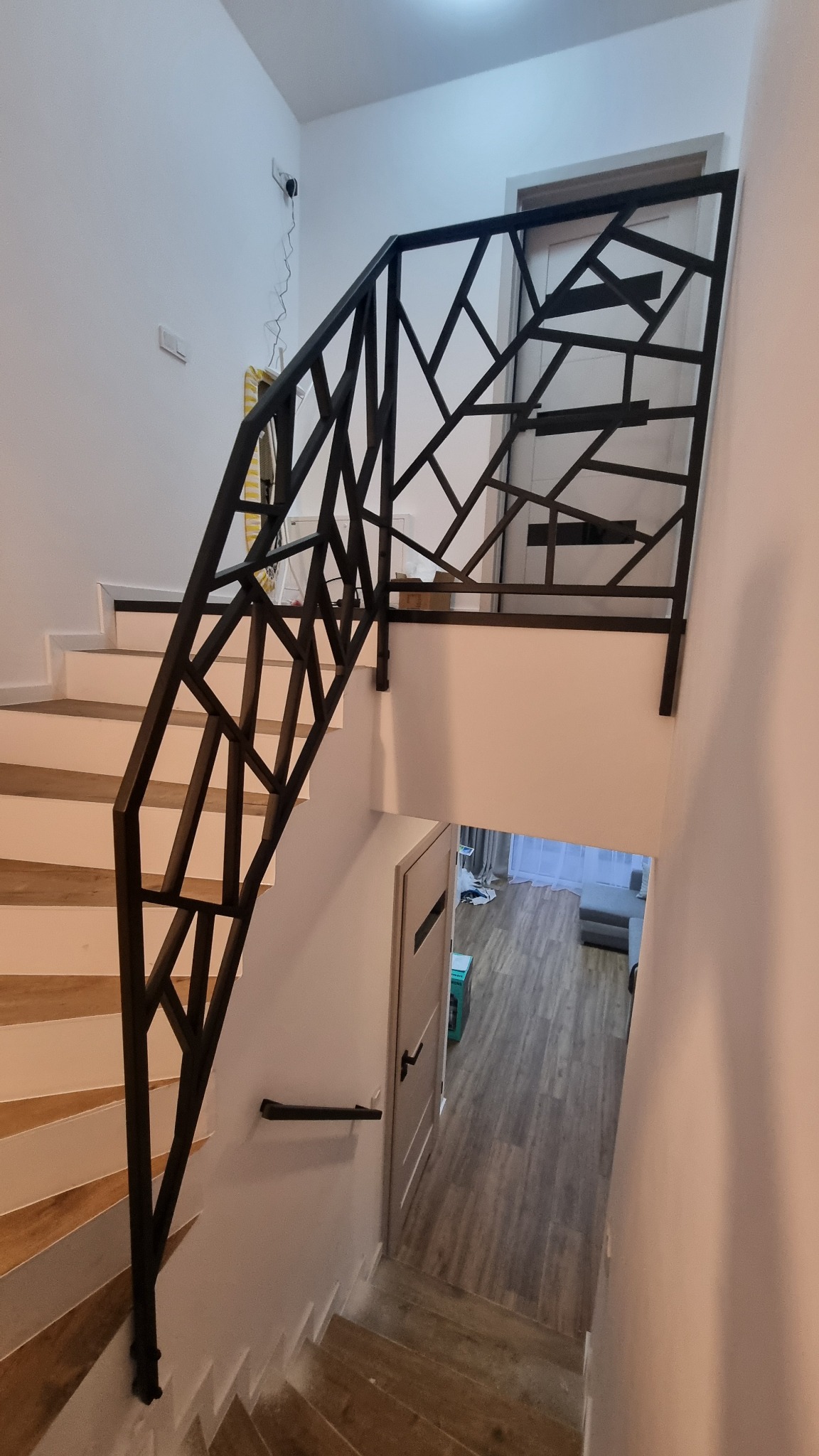 Nowoczesna balustrada schodowa z czarnego metalu o geometrycznym wzorze, widok z góry na schody i fragment korytarza. Minimalistyczny design, jasne wnętrze.
