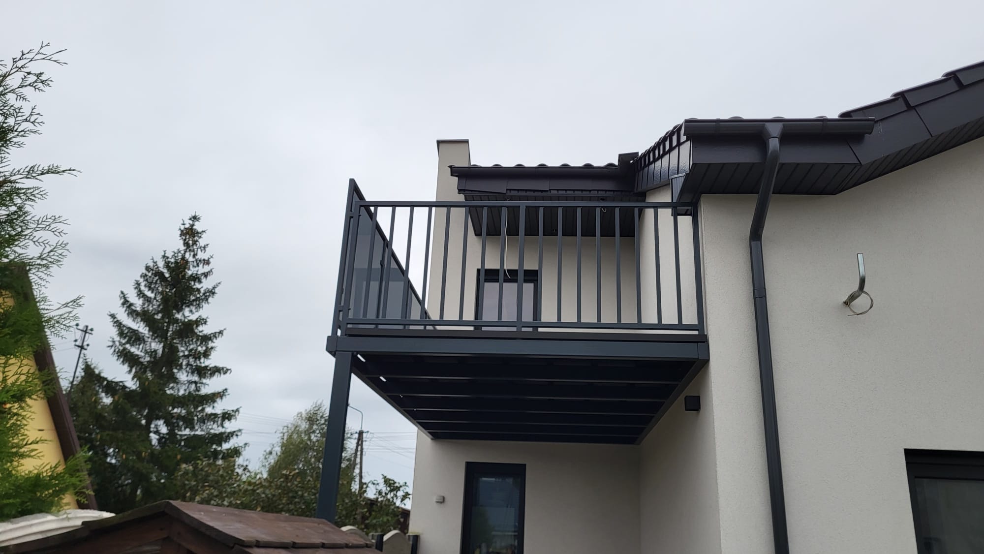 Nowoczesny balkon z czarną balustradą w Solcu Kujawskim. Metalowa konstrukcja balkonu z pionowymi szczeblami i szklanym panelem bocznym. Widok z dołu na elewację budynku.