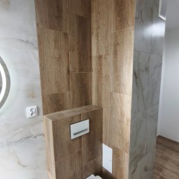 Mateusz Pencarski - Nowoczesna toaleta podwieszana w wykończonej łazience. Brązowe płytki imitujące drewno na ścianach i podłodze, marmurowe płytki na ścianie z lustrem.