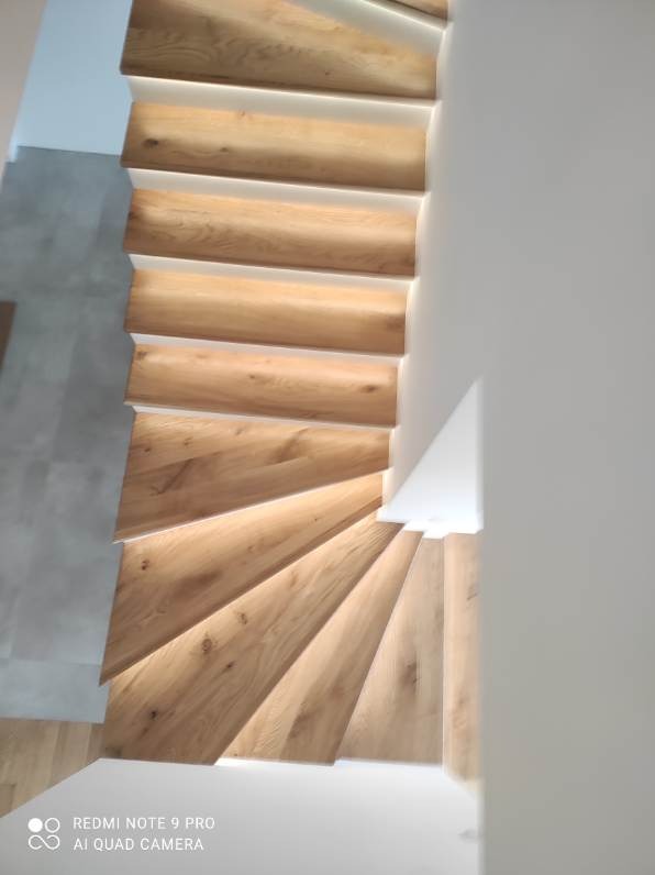 Kątowe ujęcie z góry na jasne, drewniane schody z białymi podstopnicami i subtelnym oświetleniem LED, tworzące nowoczesny i minimalistyczny design.