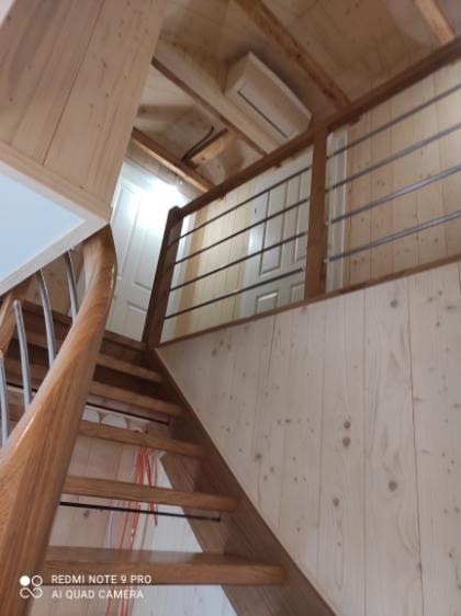 Jasne, drewniane schody z metalową balustradą w domu wykończonym boazerią. Widok z dołu, ukazujący konstrukcję i detale wykończenia.