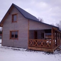 Waldemar Stasik - Zimowy krajobraz z szarym domem szkieletowym z drewnianą werandą i ciemnym dachem. Widok z boku na tle zaśnieżonego terenu i drzew.