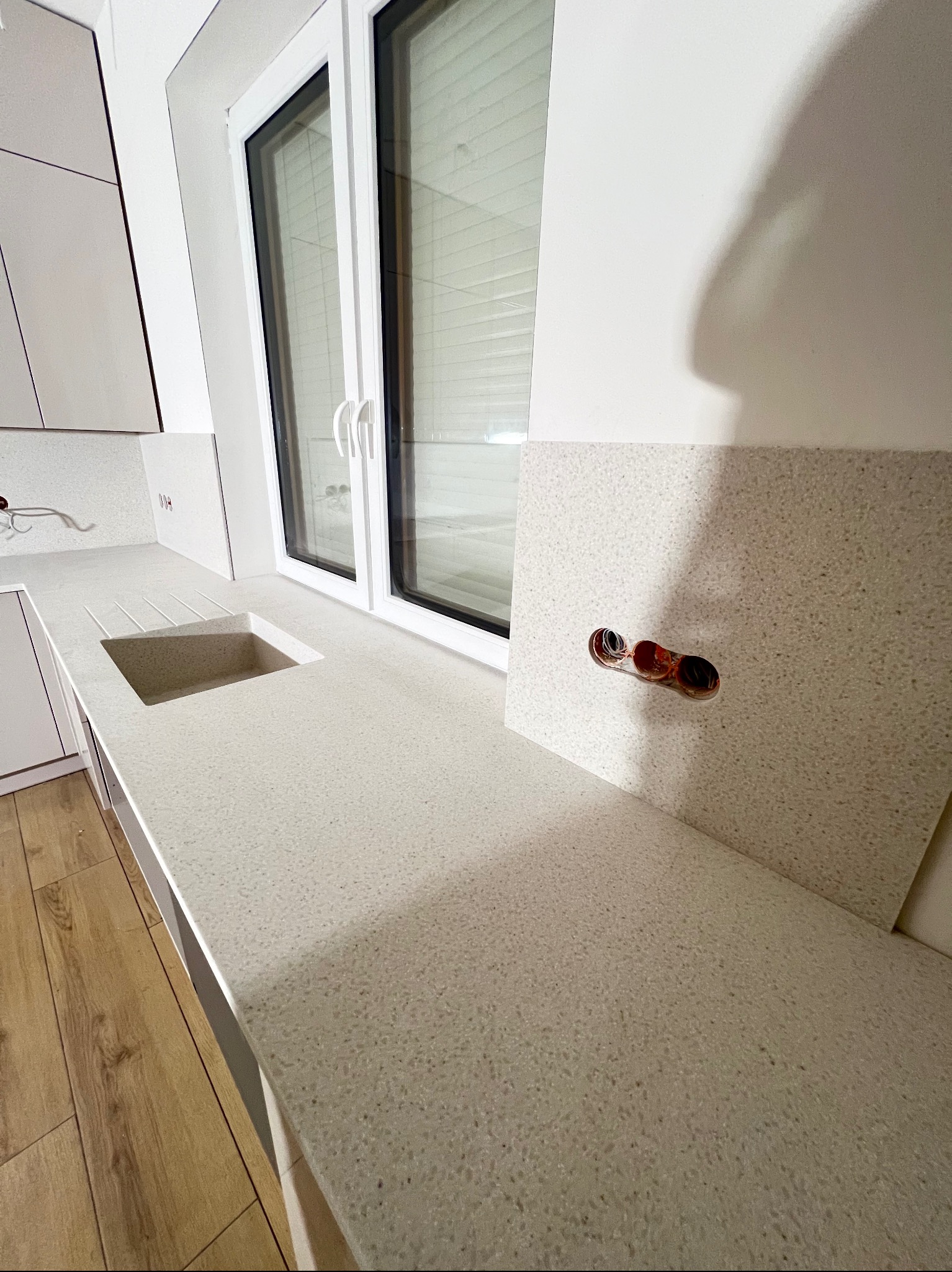 Jasny blat kuchenny z konglomeratu z wbudowanym zlewem i otworem na gniazdka elektryczne, widok z góry, nowoczesny design, drewniana podłoga w tle.