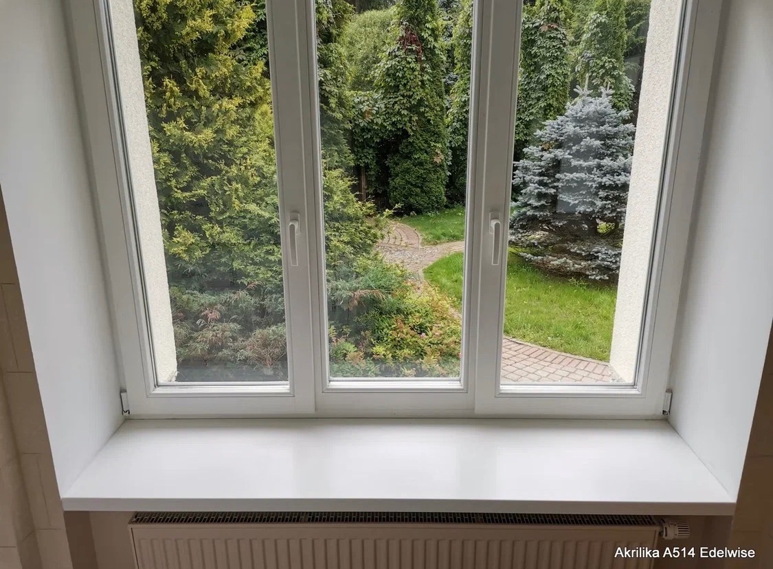 Biały parapet z PCV pod oknem z widokiem na ogród. Widoczne trzy okna z białymi ramami. Na dole grzejnik. Parapet o gładkiej powierzchni, dobrze oświetlony.