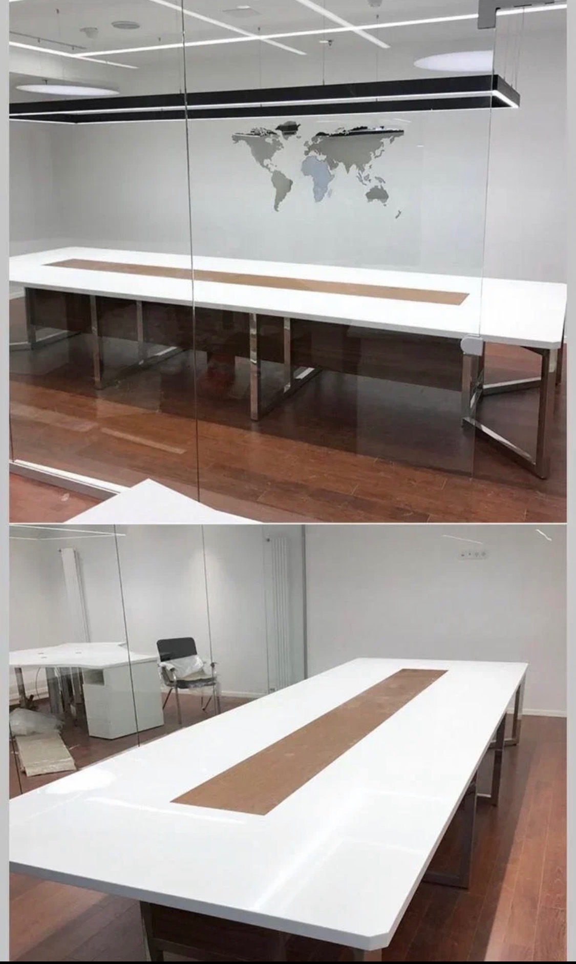 Długi, biały stół konferencyjny z drewnianym pasem pośrodku, na metalowych nogach, widziany przez szklaną ścianę w nowoczesnym biurze z mapą świata na ścianie.