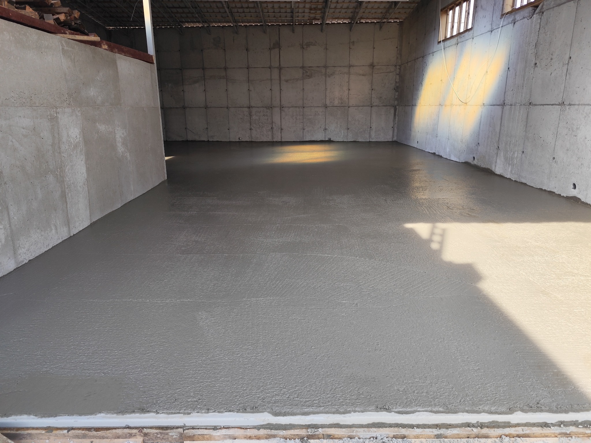 Wylana, świeża posadzka betonowa w surowym wnętrzu hali z betonowymi ścianami. Widoczne ślady po narzędziach do rozprowadzania betonu.