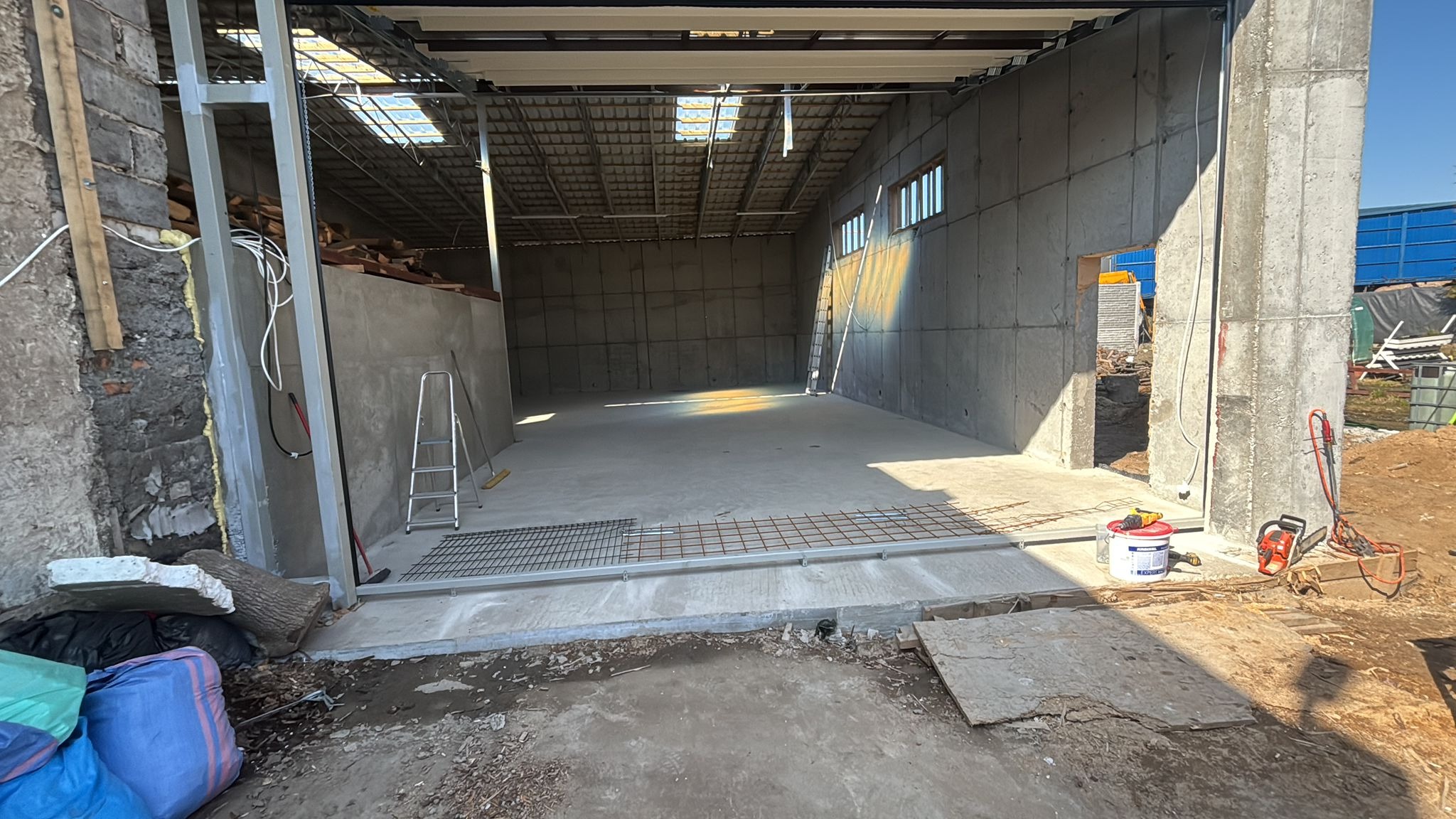 Wnętrze budowanej hali z betonu w Książkach, widoczne zbrojenie podłoża, ściany z prefabrykatów betonowych i metalowa konstrukcja dachu. Etap budowy.