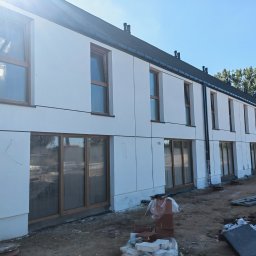 GIFTPOL Paweł Gołubców - Nowoczesny budynek w trakcie wykończenia elewacji, z widocznymi oknami z drewnianymi ramami i elementami konstrukcyjnymi. Na pierwszym planie teren budowy.