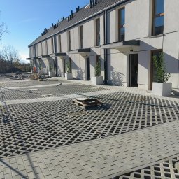 GIFTPOL Paweł Gołubców - Nowoczesne domy szeregowe z jasną elewacją i ażurowym parkingiem z kostki. Widoczne rośliny w donicach przy wejściach. Słoneczny dzień, błękitne niebo.