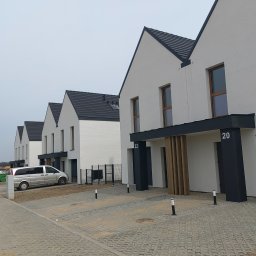 GIFTPOL Paweł Gołubców - Szereg identycznych, nowoczesnych domów z białymi elewacjami i ciemnymi dachami, z numerami 20 i 22, widzianych z perspektywy ulicy, w tle plac budowy.