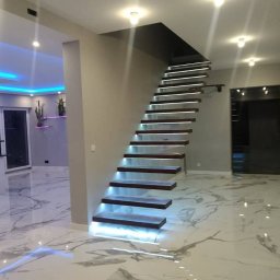 MG builders design company - Nowoczesne schody z podświetleniem LED i marmurową podłogą w przestronnym wnętrzu. Minimalistyczny design, eleganckie wykończenie, subtelne oświetlenie.