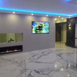 MG builders design company - Nowoczesny salon z marmurową podłogą, podświetlanym sufitem LED, kominkiem i telewizorem z motywem akwarium. Ściana z kamienia dekoracyjnego.