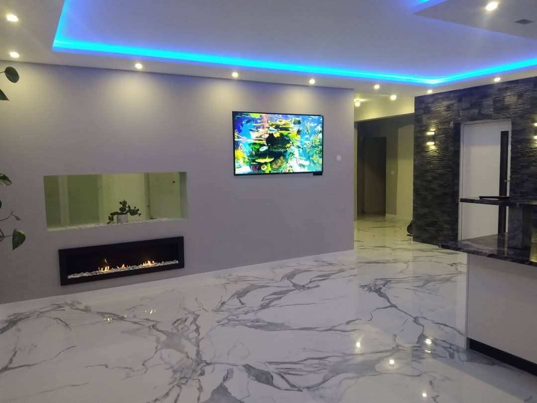 Nowoczesny salon z marmurową podłogą, podświetlanym sufitem LED, kominkiem i telewizorem z motywem akwarium. Ściana z kamienia dekoracyjnego.