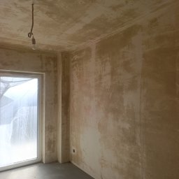 KRIS-BUD - Pokój w trakcie przygotowania do malowania: surowe ściany z widocznymi śladami szpachlowania, okno zabezpieczone folią, sufit z wiszącą żarówką. Stan deweloperski.