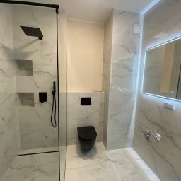 KRIS-BUD - Nowoczesna łazienka z kabiną typu walk-in, wykończona białym marmurem, czarną armaturą i podświetlanym lustrem. Minimalistyczny design z akcentami czerni.
