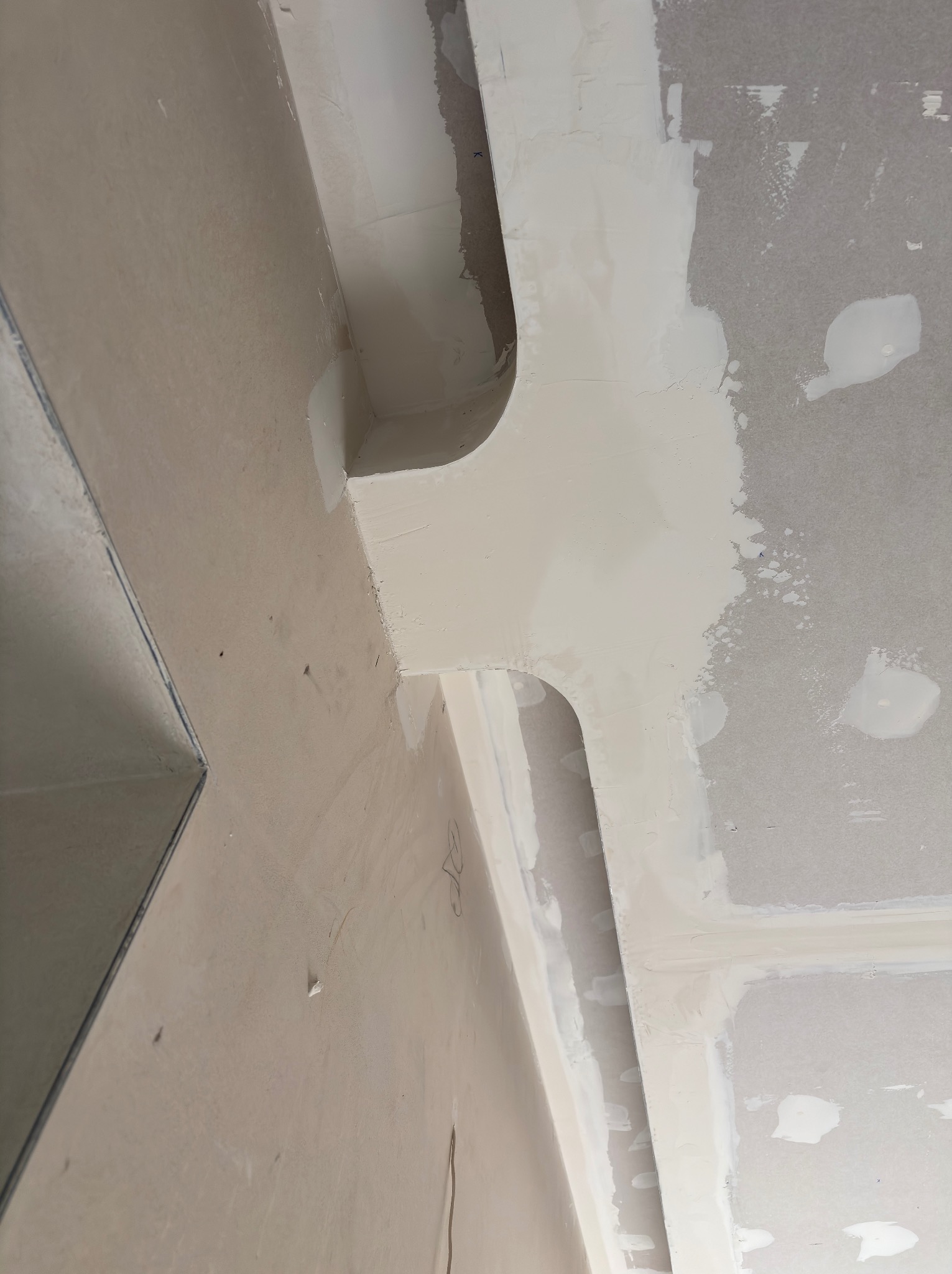 Sufit z płyt gipsowo-kartonowych, częściowo wyszpachlowany, z widocznymi łączeniami i narożnikami. Ujęcie z dołu, pod kątem, ukazujące etap prac wykończeniowych.