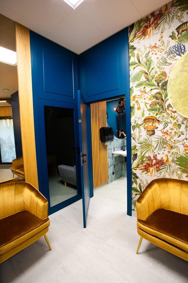 Niebieskie drzwi wewnętrzne z ościeżnicą w nowoczesnym wnętrzu z wzorzystą tapetą i złotymi fotelami, widok na sąsiednie pomieszczenia.