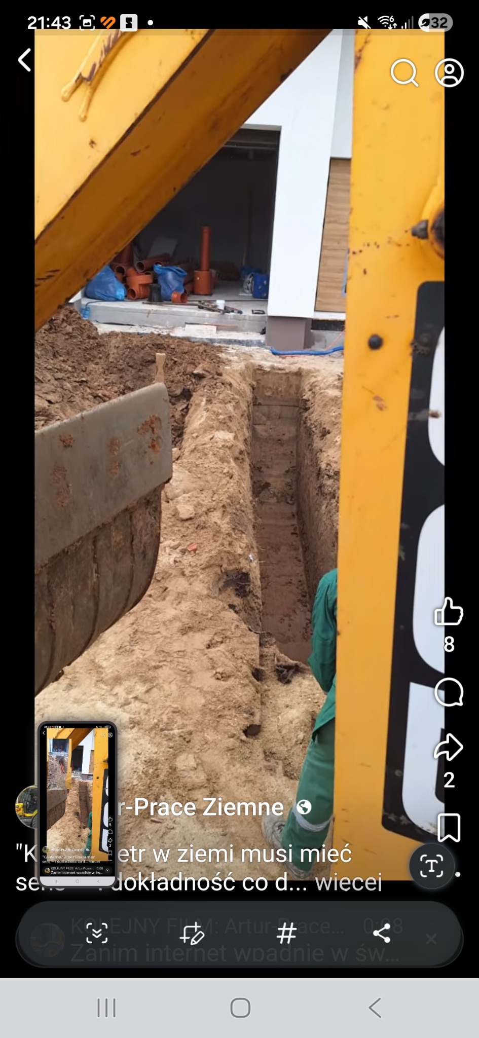 Wąski wykop w ziemi, wykonany prawdopodobnie pod instalacje, widziany z perspektywy koparki. W tle widoczne elementy budynku i rury.