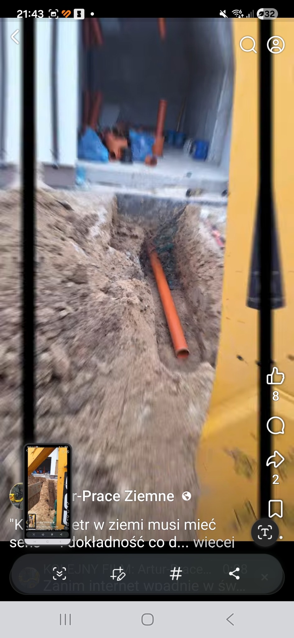 Wykopany rów z pomarańczową rurą w ziemi, widoczny fragment koparki. W tle materiały budowlane. Ujęcie z bliska, z perspektywy ziemi.