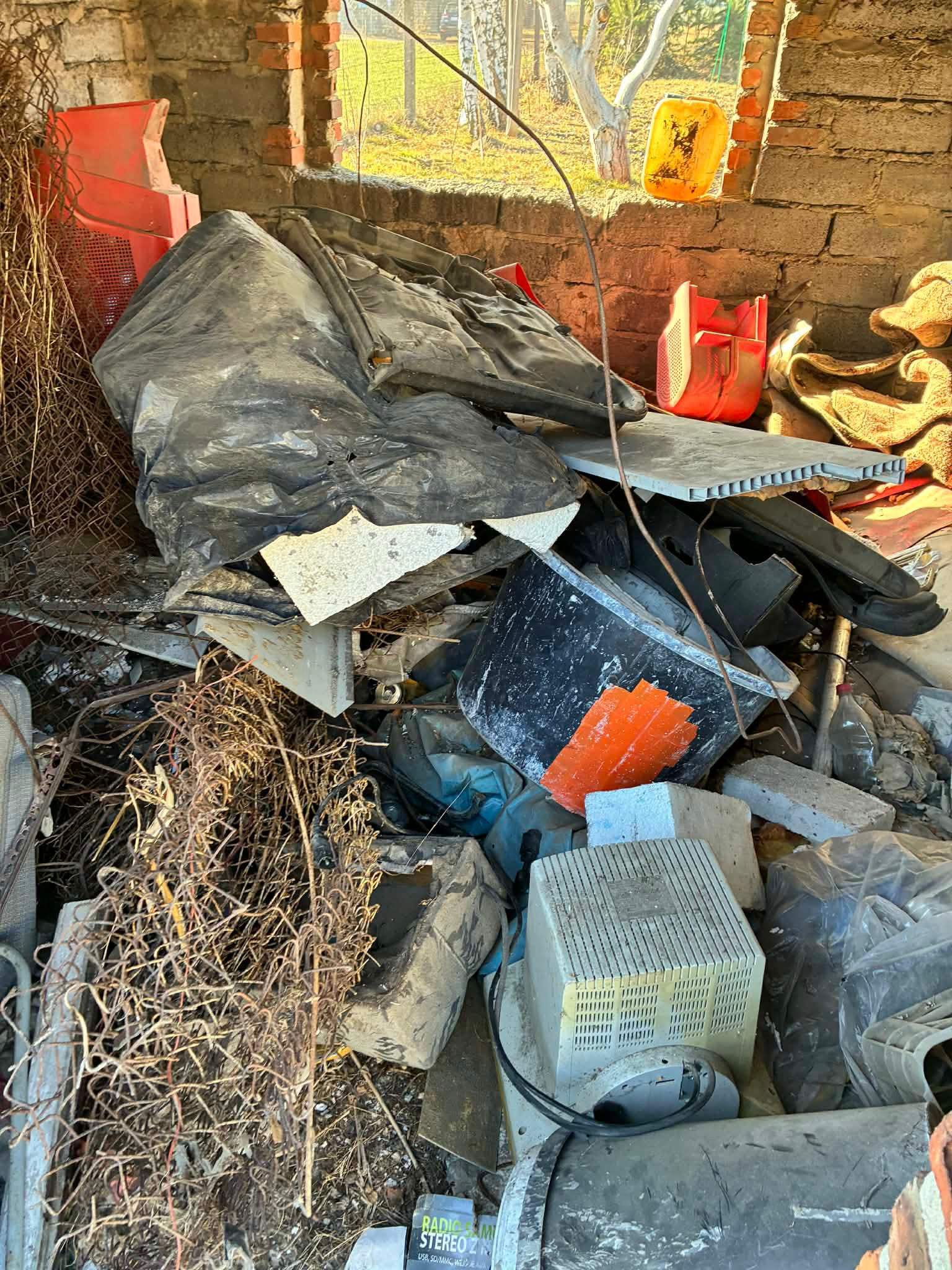Stary monitor CRT, gruz, metalowa siatka i plastikowe pojemniki w pomieszczeniu z ceglanymi ścianami. Opróżnianie pomieszczenia ze zbędnych przedmiotów.