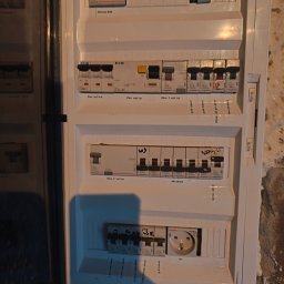 Piotr Żebrowski - Otwarta biała rozdzielnica elektryczna z rzędami zabezpieczeń Legrand i EATON, wyraźnie opisanych jako obwody pieca, zmywarki, oświetlenia i gniazd, z widocznym wskaźnikiem LK-713.