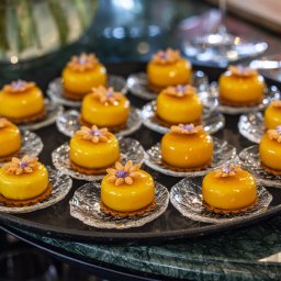 Concordia Design Catering - Eleganckie, żółte mini-desery z kwiatami na kruchym spodzie, ułożone na szklanych talerzykach na czarnej tacy. W tle rozmyte szkło i marmurowy blat.