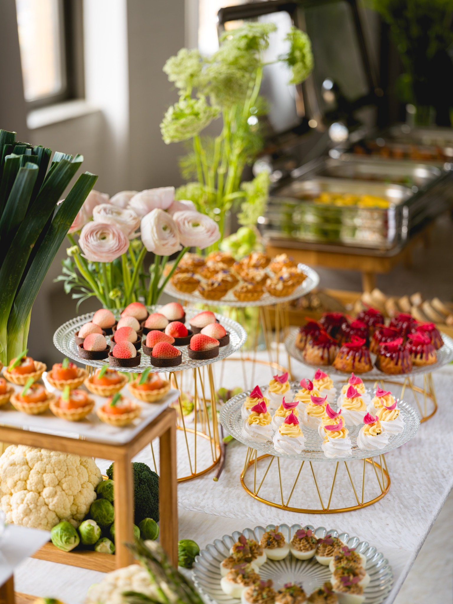 Elegancki stół cateringowy z różnorodnymi przekąskami: tartaletki z łososiem, mini bezy z kremem, jajka faszerowane, desery truskawkowe i kwiatowe dekoracje.