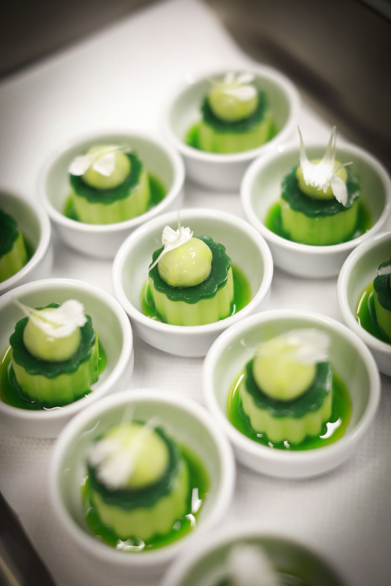 Eleganckie, zielone desery w białych miseczkach, udekorowane kwiatami, tworzące apetyczną kompozycję. Idealne na wykwintne przyjęcie lub firmowy event.