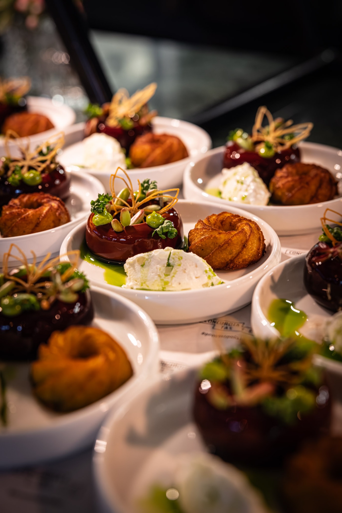 Eleganckie przystawki cateringowe: mini babeczki i błyszczące desery z kremem, udekorowane zieleniną i orzechami, podane na białych talerzykach. Wyrafinowany catering.