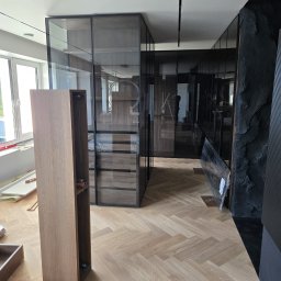 PRESTIGE DECOR ROBERT MOCZULSKI - Montaż szklanej szafy wnękowej z drewnianymi elementami w nowoczesnym wnętrzu z parkietem w jodełkę i dekoracyjną ścianą z kamienia.