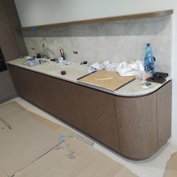 PRESTIGE DECOR ROBERT MOCZULSKI - Montaż kuchni na wymiar: zabudowa z drewnianymi frontami i marmurowym blatem, widoczne narzędzia i materiały montażowe, podłoga zabezpieczona kartonem.