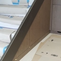 PRESTIGE DECOR ROBERT MOCZULSKI - Fragment zabudowy schodów z drewnopodobnej płyty, widoczne zabezpieczone schody i fragment szafy wnękowej. Ujęcie z dołu, z bliska, w trakcie prac wykończeniowych.