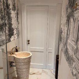 Sławomir Grządziel - Elegancka łazienka z marmurową umywalką wolnostojącą, białą stolarką i tapetą w stylu retro. Umywalka z beżowego marmuru, złota armatura.