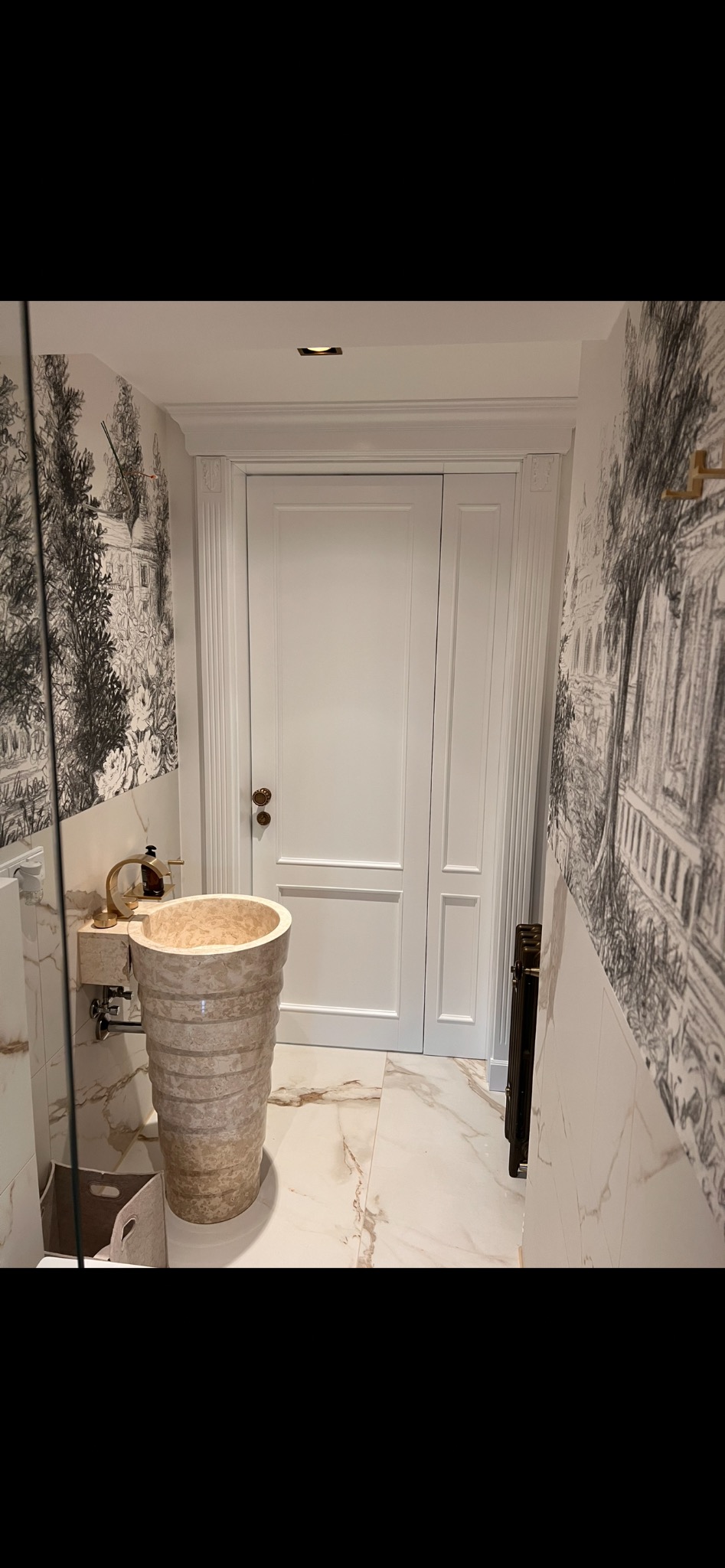 Elegancka łazienka z marmurową umywalką wolnostojącą, białą stolarką i tapetą w stylu retro. Umywalka z beżowego marmuru, złota armatura.