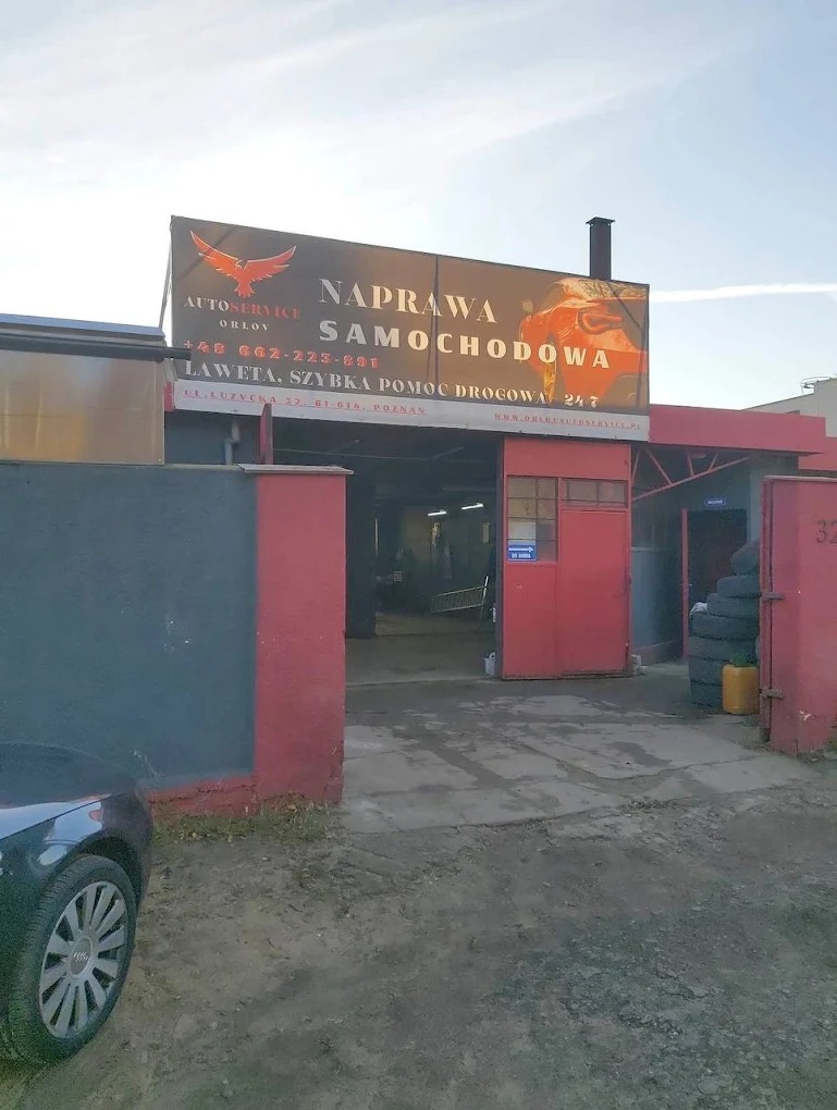 Fasada warsztatu samochodowego Orlov z szyldem 'Naprawa Samochodowa, Laweta, Szybka Pomoc Drogowa 24/7' i częściowo widocznym autem na pierwszym planie.