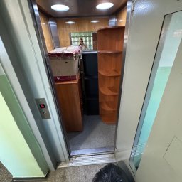 OpróżnijTo - Wnętrze windy załadowanej meblami i kartonami podczas przeprowadzki. Widoczny przycisk z numerem piętra '5' i czarny worek na podłodze.