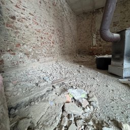 OpróżnijTo - Wnętrze po wyburzeniu: gruz, fragmenty cegieł i instalacji. Widoczne ślady po ścianach i instalacjach. Ujęcie z bliska, podkreślające surowość stanu po demontażu.