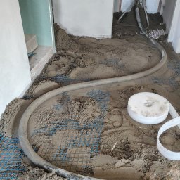 Gaw-Bud Posadzki maszynowe - Wylewka jastrychowa w trakcie realizacji: szara masa na siatce z rurą doprowadzającą, widoczne ślady stóp. Surowe ściany i instalacje elektryczne w tle.