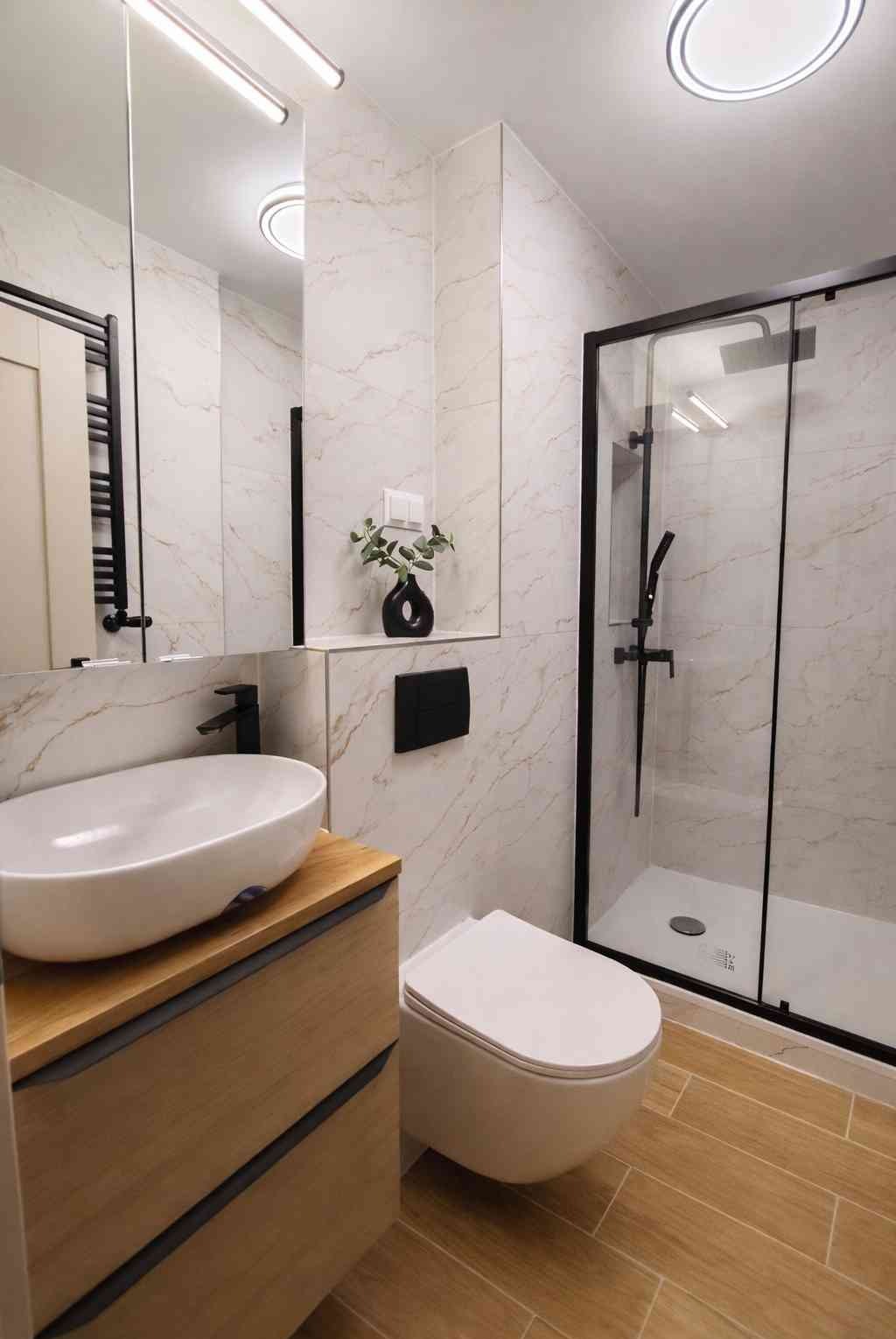 Nowoczesna łazienka z kabiną prysznicową typu walk-in, umywalką nablatową na drewnianej szafce i marmurowymi płytkami ściennymi z delikatnym złotym żyłkowaniem.