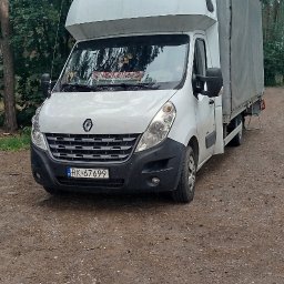 Zenik-Trans- Zenon Burdzy - Biały Renault Master z plandeką na leśnej drodze. Widoczna tablica rejestracyjna i naklejka 'Polska' na przedniej szybie. Ujęcie z dołu, drzewa w tle.