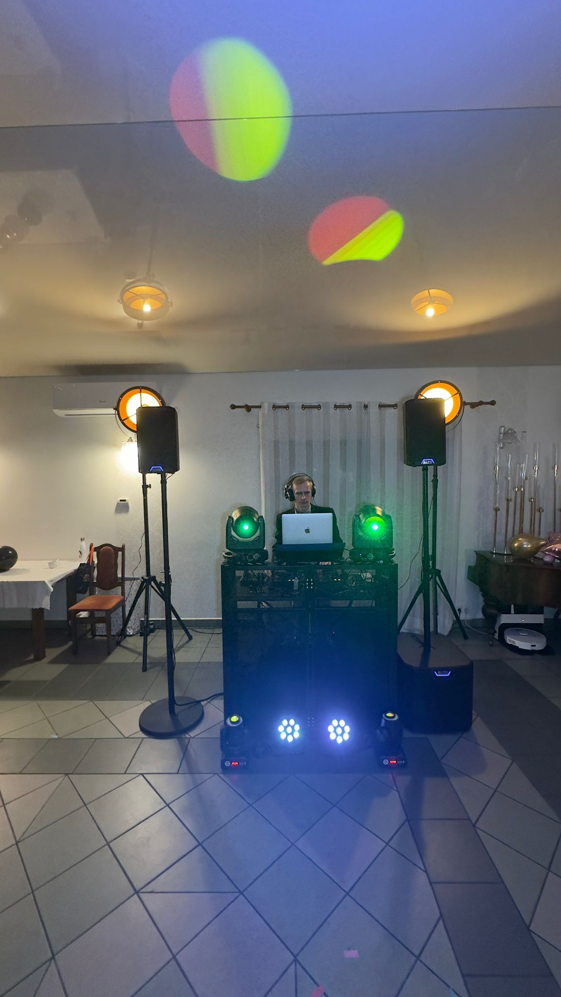 DJ z laptopem i słuchawkami za konsoletą, oświetlenie sceniczne w tle, światła punktowe na suficie. Sprzęt nagłośnieniowy i oświetleniowy podczas imprezy.