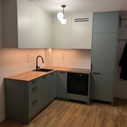 Grzegorz Augustynek - Szara kuchnia na wymiar z drewnianym blatem i czarną armaturą. Górne szafki białe, oświetlenie LED pod szafkami. Na podłodze panele imitujące drewno.