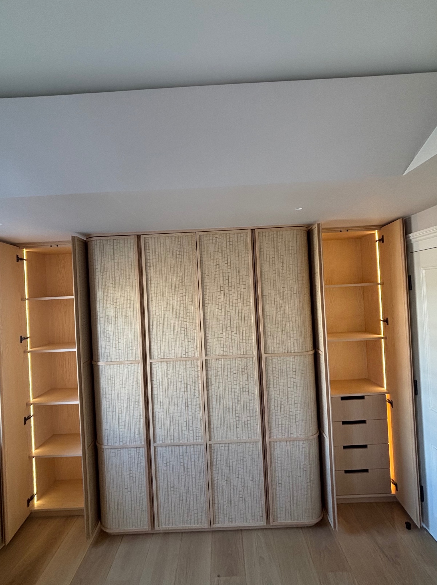 Wnętrze szafy wnękowej z oświetleniem LED, widoczne półki i szuflady. Fronty szafy z unikalną, teksturowaną okleiną w odcieniach beżu i brązu. Jasna podłoga.