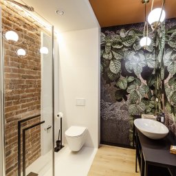 AWPLUS Architektura wnętrz Maja Staniszewska - Nowoczesna łazienka z kabiną prysznicową, ceglaną ścianą i tapetą w liście. Umywalka nablatowa na czarnej konsoli. Oświetlenie punktowe i wiszące lampy.
