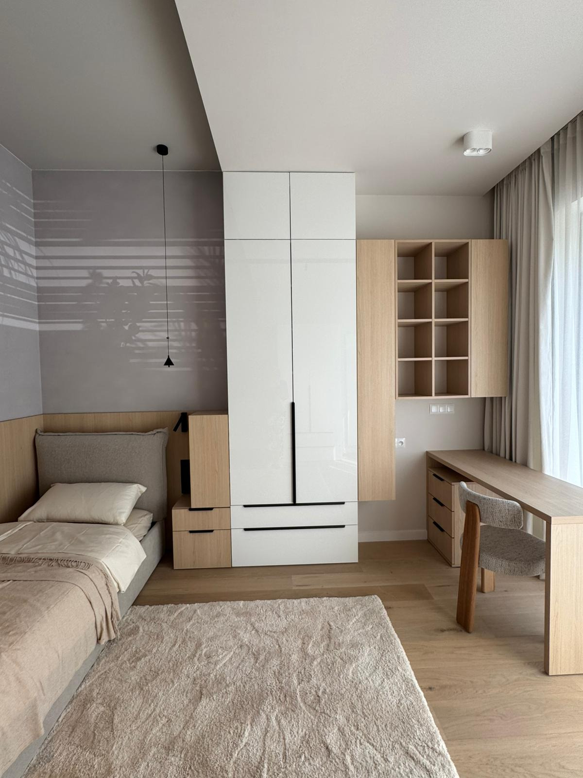 Nowoczesna aranżacja pokoju z łóżkiem, biurkiem i szafą w zabudowie, w jasnych barwach. Minimalistyczny design w Polanicy-Zdroju. Subtelne oświetlenie i naturalne materiały.