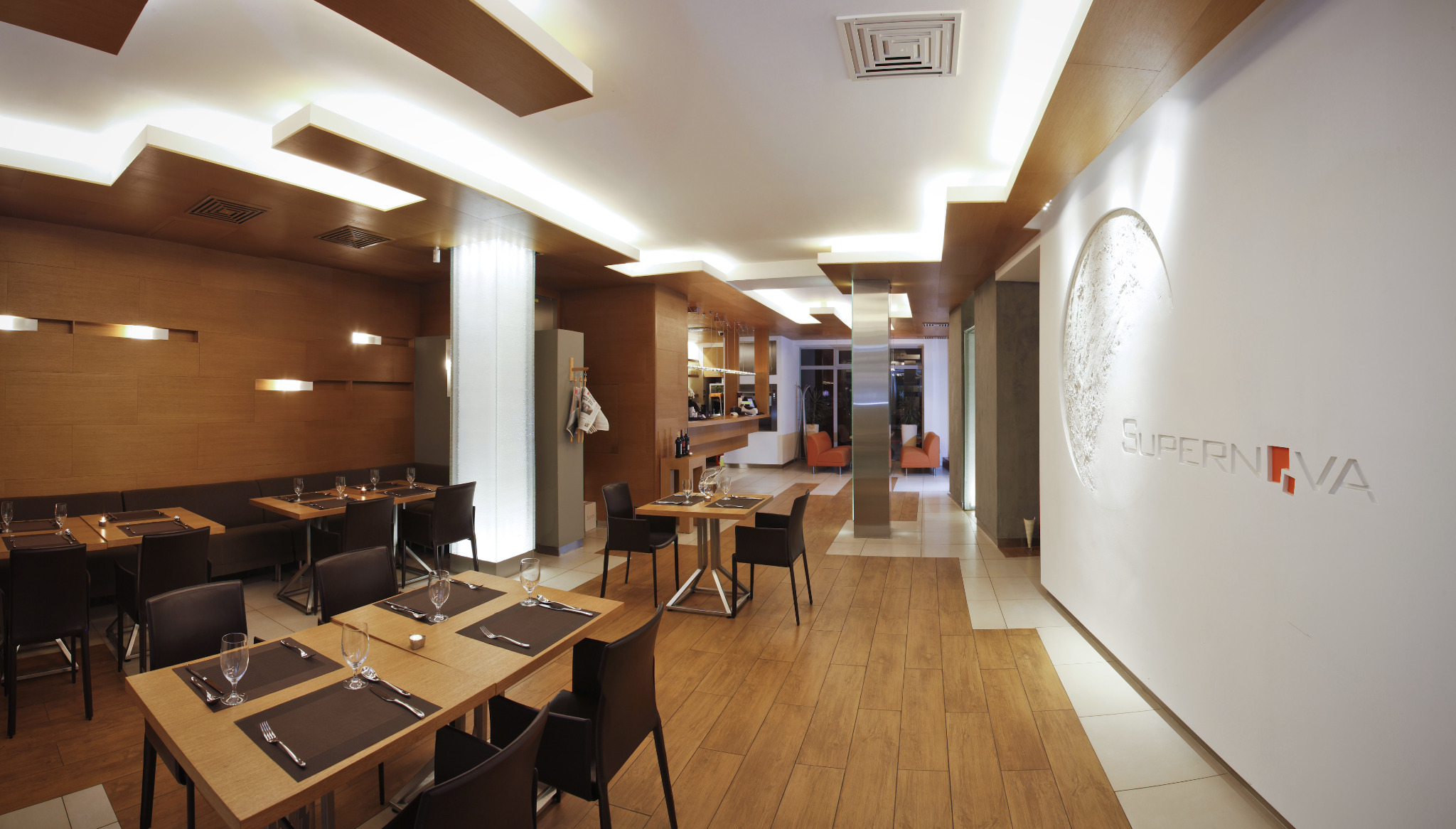 Eleganckie wnętrze restauracji z drewnianymi stołami nakrytymi dla gości, oświetleniem sufitowym i dekoracyjną ścianą z logo.