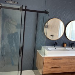 Norbert Gębuś Firma Budowlana LEOŚ - Nowoczesna łazienka z kabiną prysznicową typu walk-in, drewnianą szafką z umywalkami i okrągłymi lustrami na tle ściany z geometrycznym wzorem.