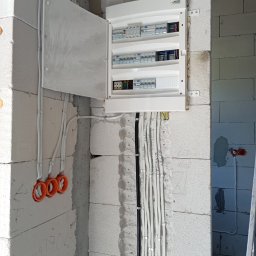 Usługi Elektryczne - Otwarta skrzynka elektryczna z bezpiecznikami na ścianie z betonu komórkowego. Widoczne kable w peszlach i oznaczenia na ścianie. Instalacja w trakcie prac.